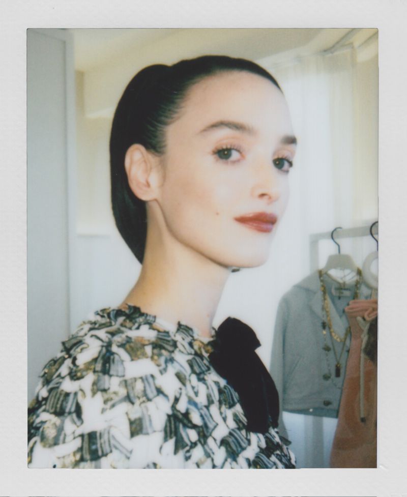 Portrait of an adult woman with dark hair pulled back, wearing a patterned top, looking to the side in a soft, indoor setting.