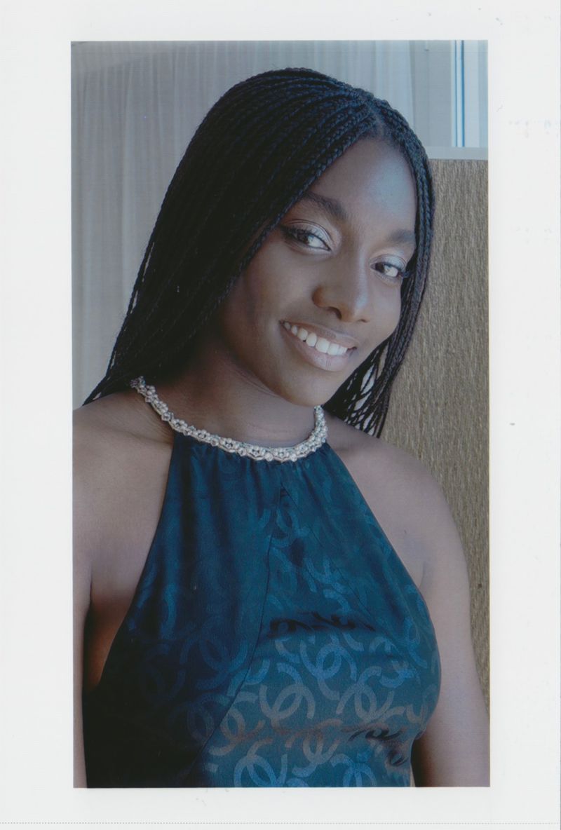 A beautiful Black woman smiles in a close-up studio portrait. She's wearing a dress with a beaded collar. The background is soft and neutral.
