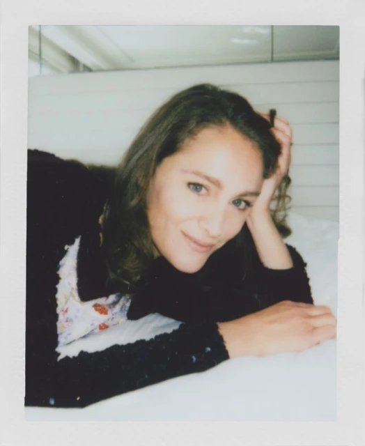 Portrait of a woman with long brown hair smiling while laying on a white surface. Indoor setting with natural, soft lighting.