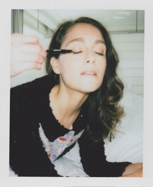 Woman receiving makeup applied to her eyelashes. One adult female with eyes closed, makeup artist applying mascara on indoor setting.