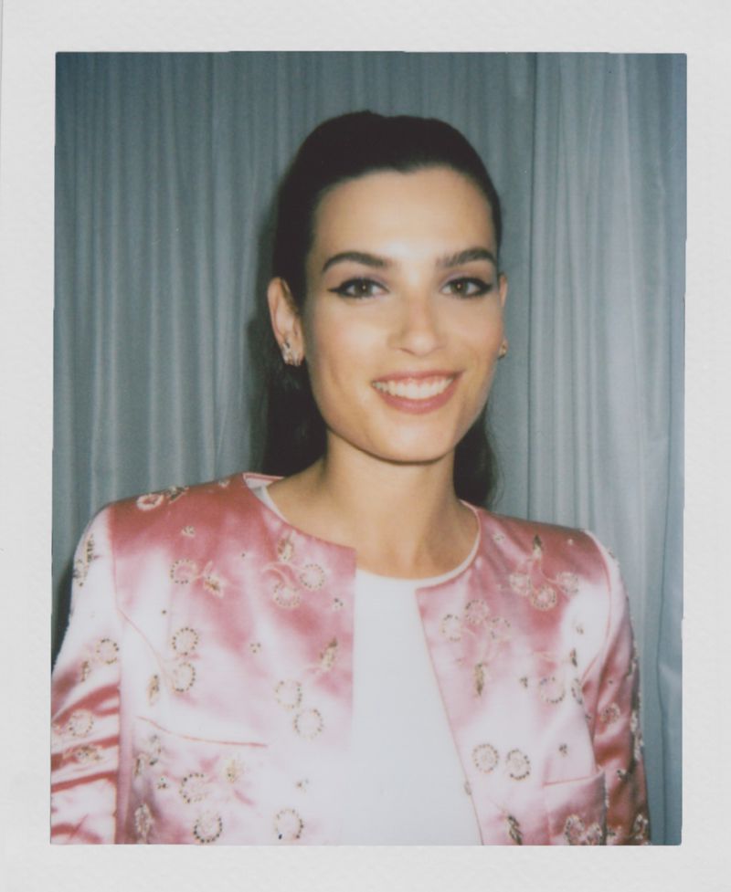Close-up portrait of a smiling woman in a pink jacket against a draped background, with studio lighting and a focus on facial features.