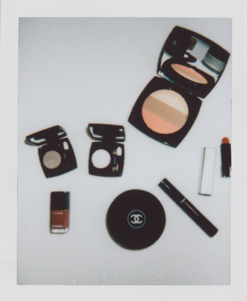 Composition of Chanel makeup products and nail polish in brown and black, arranged on a light surface in a polaroid-style frame.