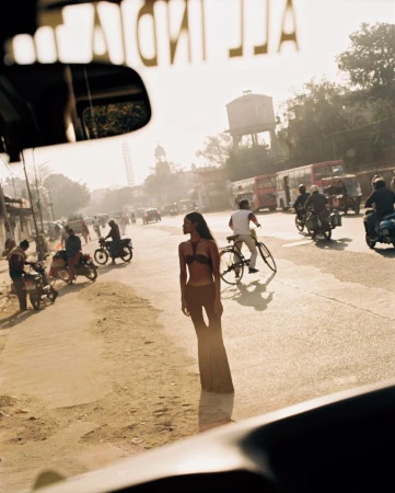 Outdoor shot of a woman in a bikini and pants standing in a street in India with buses, motorbikes, and people in the background.