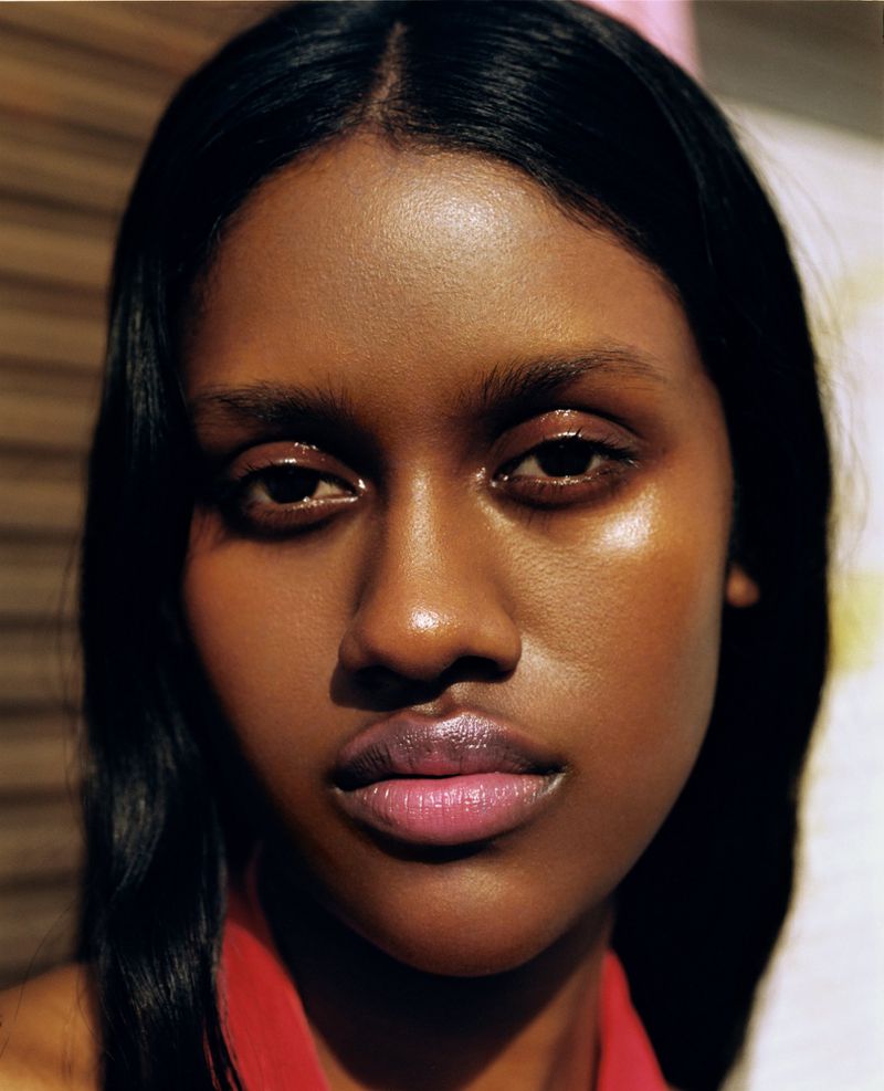 Close-up portrait of an adult Black woman with long dark hair and pink lips, highlighted by soft, diffused lighting and shallow depth of field.