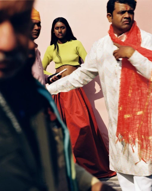 Fashion shot featuring a woman in a yellow crop top and red skirt, posing outdoors with several other adults in traditional clothing.