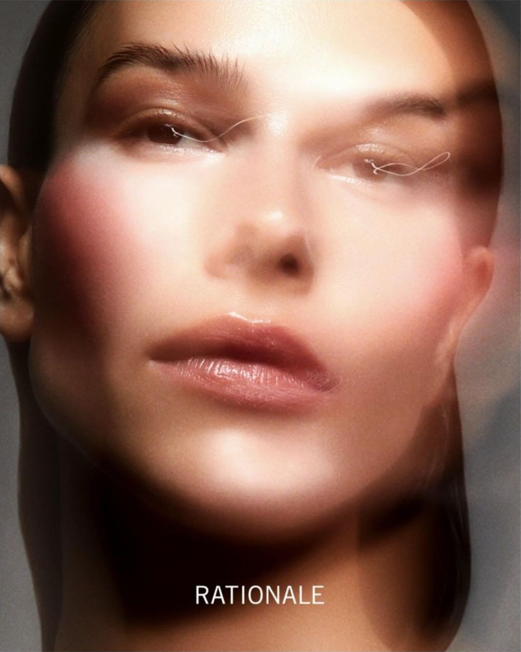 Close-up studio shot of an adult female's face featuring glossy lips, delicate eye makeup, and soft lighting against a neutral backdrop.