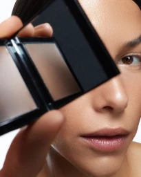Close-up portrait of a model holding a compact mirror covering one eye for Rationale