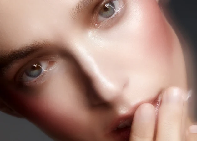Close-up beauty portrait of a woman with glowing skin and flushed cheeks touching her lips for Rationale.