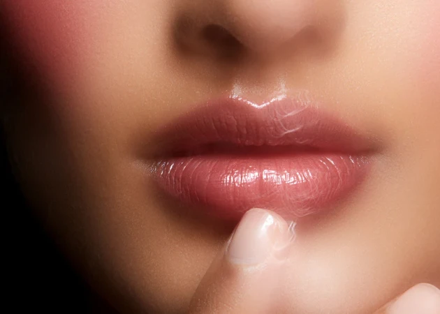 Close-up of glossy lips and chin being touched by a finger for Rationale The Beautiful Balm Collection