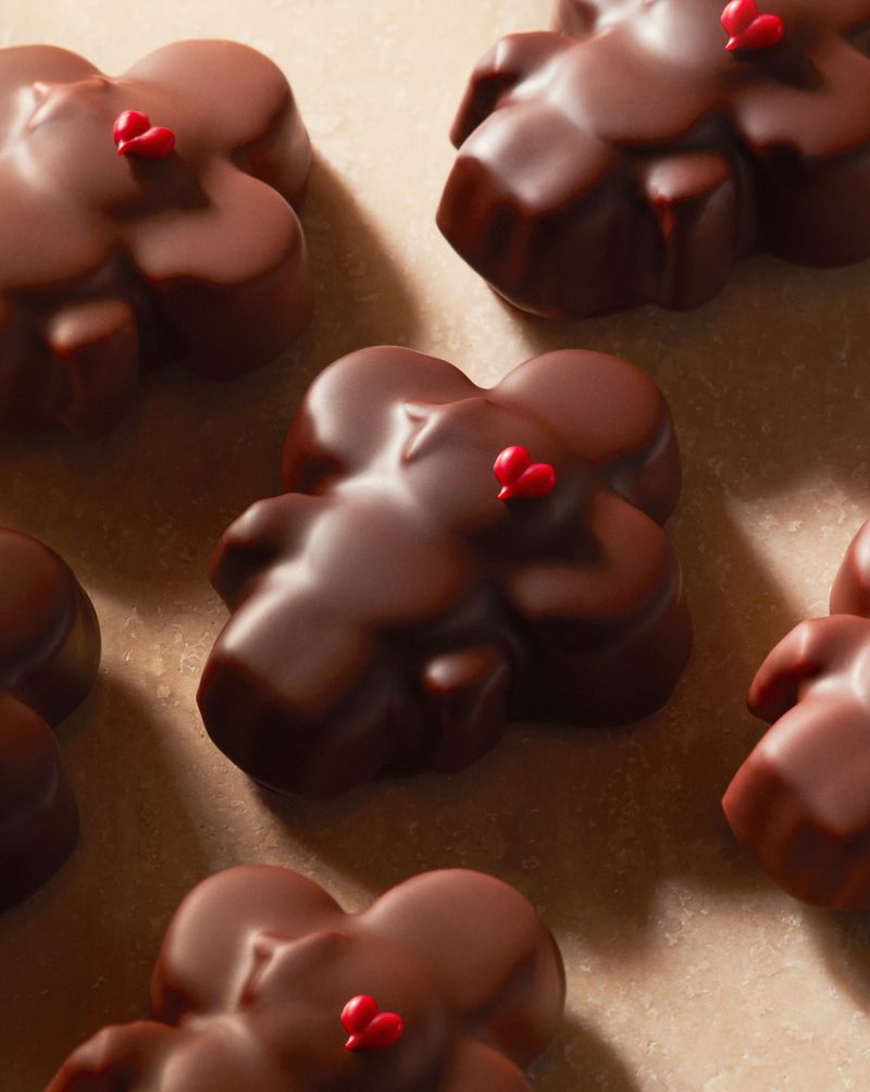 Several flower-shaped chocolates with small red sprinkles are arranged on a beige surface, creating a delicious and visually appealing pattern.