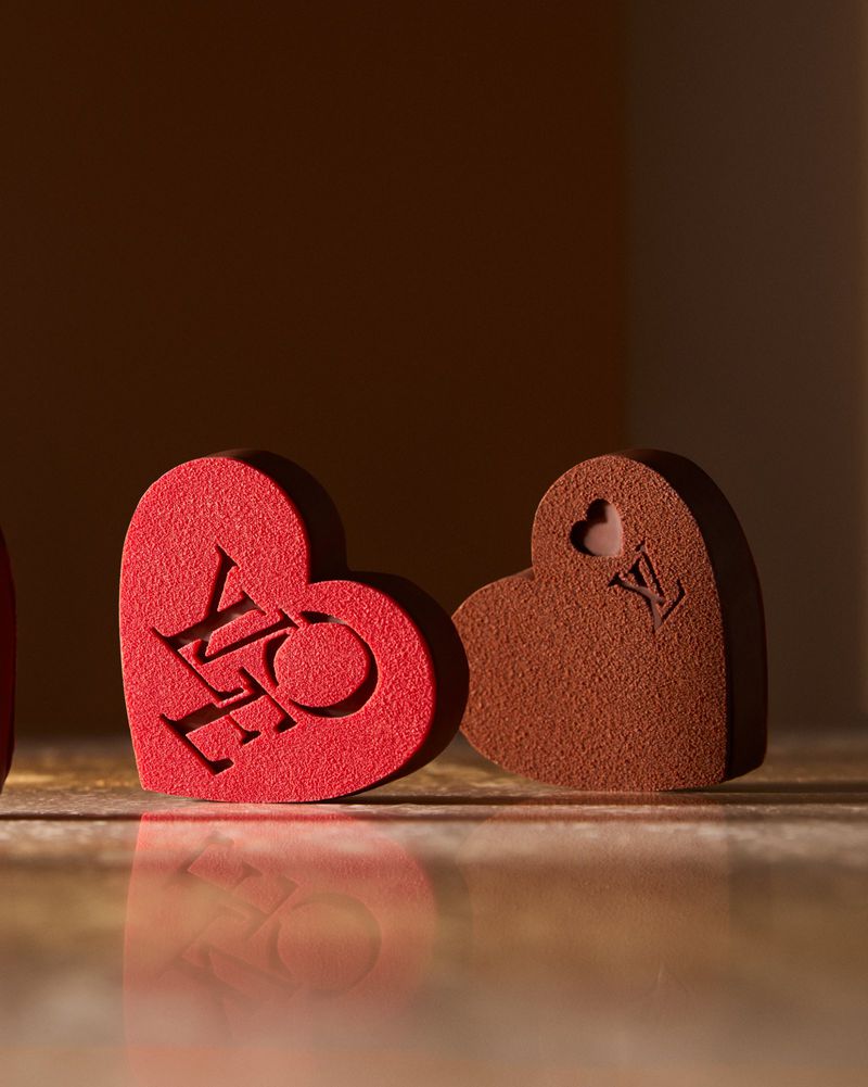 Three heart-shaped objects, one red with 'LOVE' carved, another brown with a logo, against a diffused brown background.