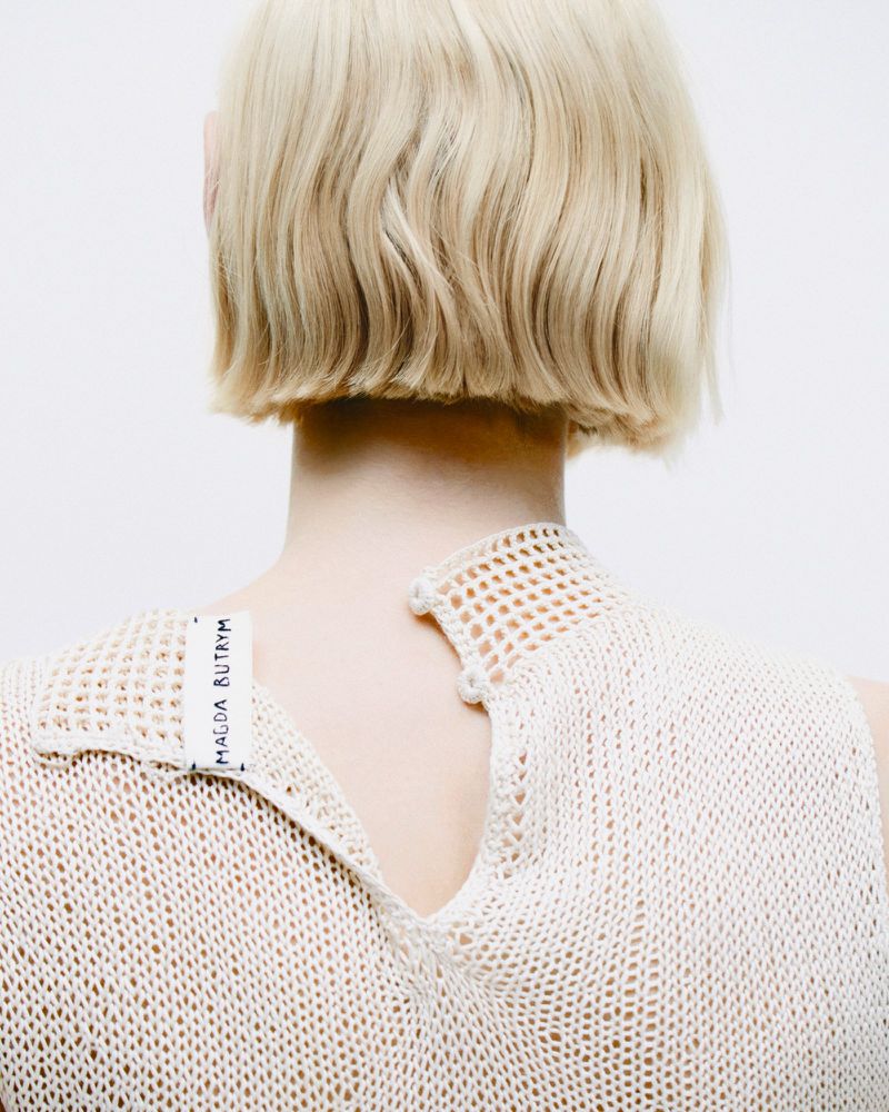 Back view of woman with blond bob haircut wearing a cream knitted top against a white background, fashion editorial studio shot.