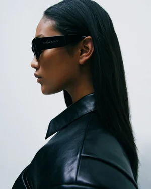 Model in profile wearing black sunglasses and black leather jacket against a light background