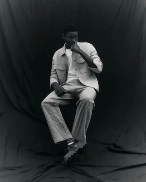 Seydou Sarr seated wearing a button-up jacket and trousers against a dark backdrop for Vogue Italia editorial photography