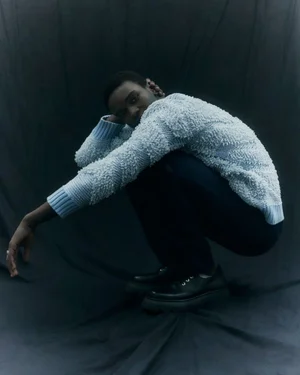Seydou Sarr squatting in a textured light blue sweater against a dark backdrop for Vogue Italia, photographed by Gautier Pellegrin.