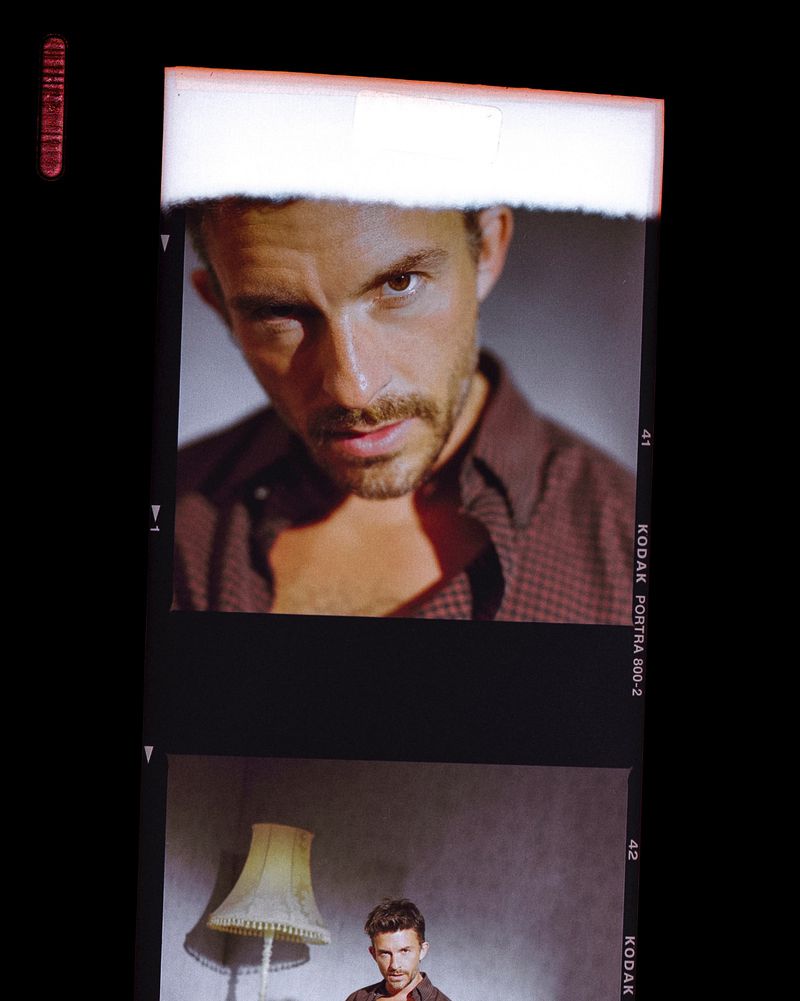 Portrait of a man in a red patterned shirt, shown as a film strip frame, with a light fixture visible in a smaller frame.