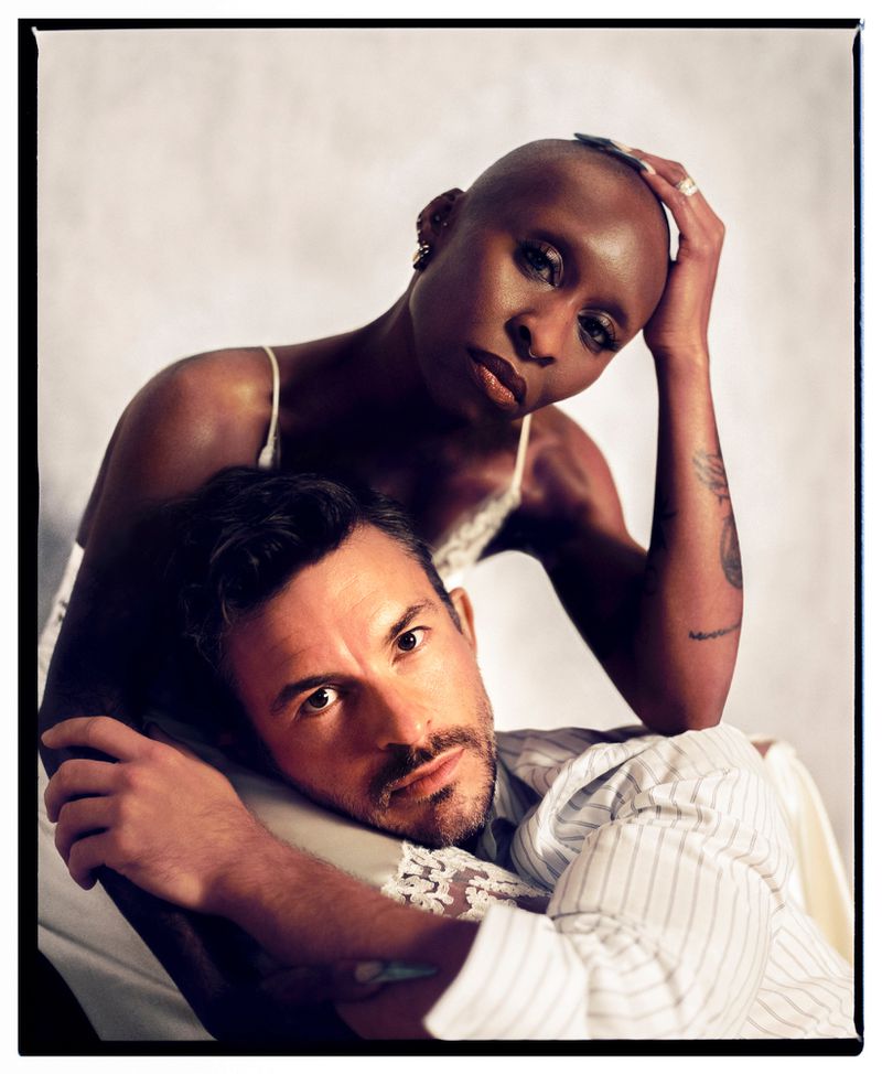 Portrait of a mixed race couple in a photo studio. The woman is bald and has dark skin. The man has dark hair and a white and blue striped shirt.