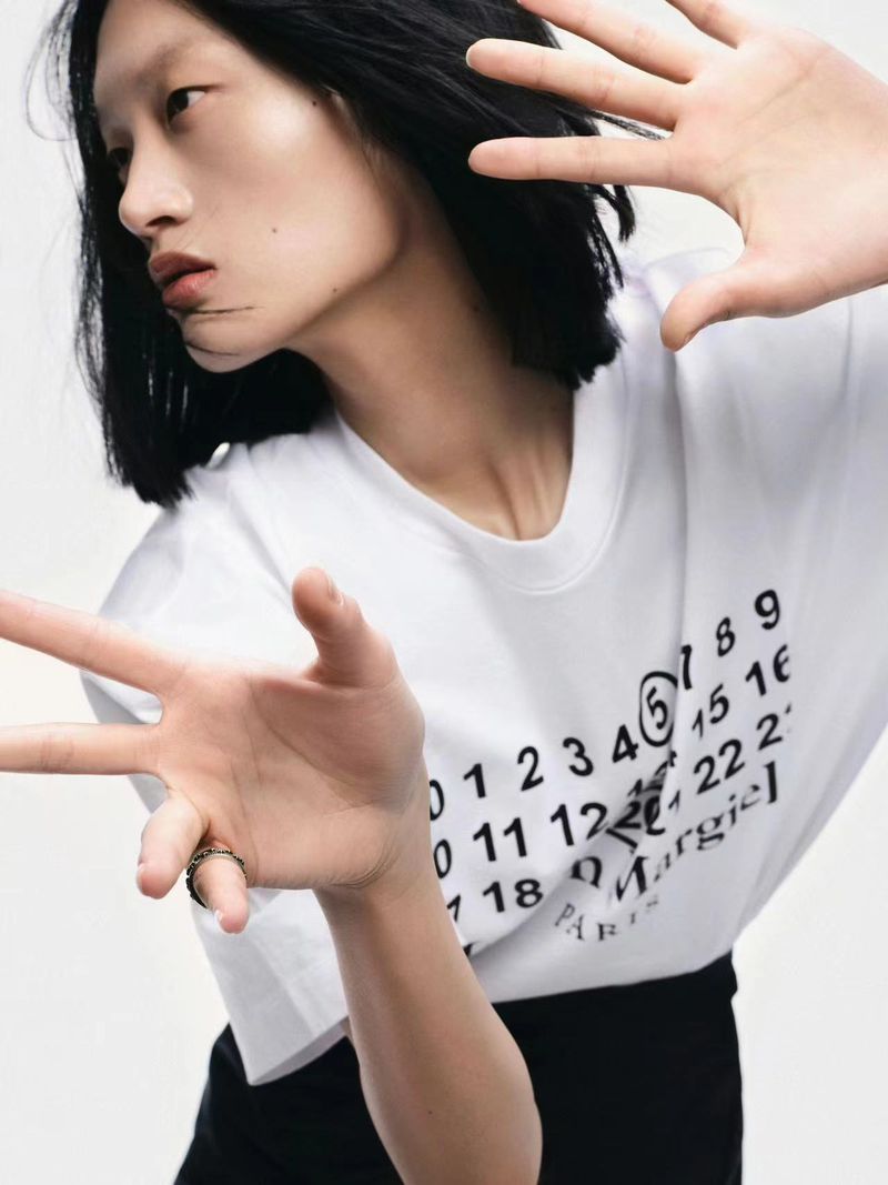 Asian woman with hands up, wearing a printed white t-shirt and black skirt, posing in a studio. Fashion editorial photography.