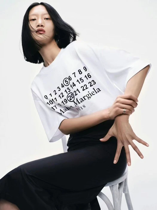 Model Yilan Hua wearing a white Maison Margiela t-shirt and black skirt against a white studio background.
