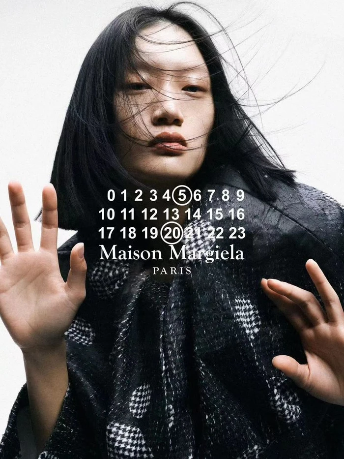 Model Yilan Hua wearing a dark patterned jacket pressed against a transparent surface for Maison Margiela.