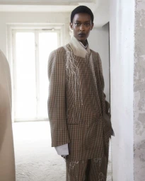 Model wearing a patterned tailored blazer and trousers with fringed detailing standing indoors