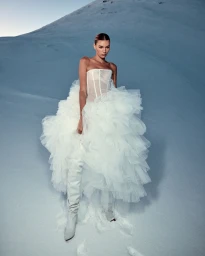 Model in white strapless tulle gown and tall boots standing against a snowy slope