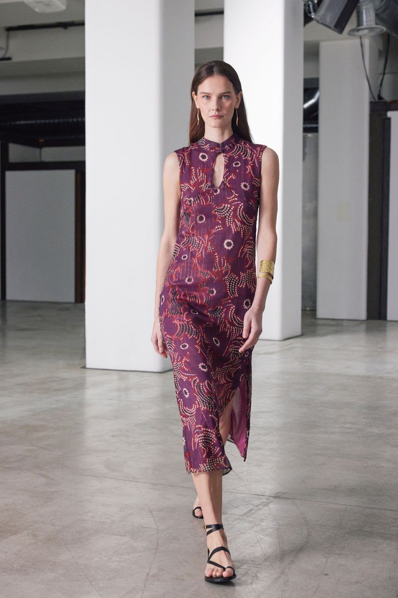 Fashionable woman in a plum sleeveless midi dress with an abstract print and strappy sandals in a light industrial interior.