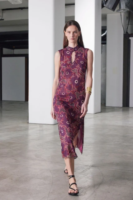 Fashionable woman in a plum sleeveless midi dress with an abstract print and strappy sandals in a light industrial interior.