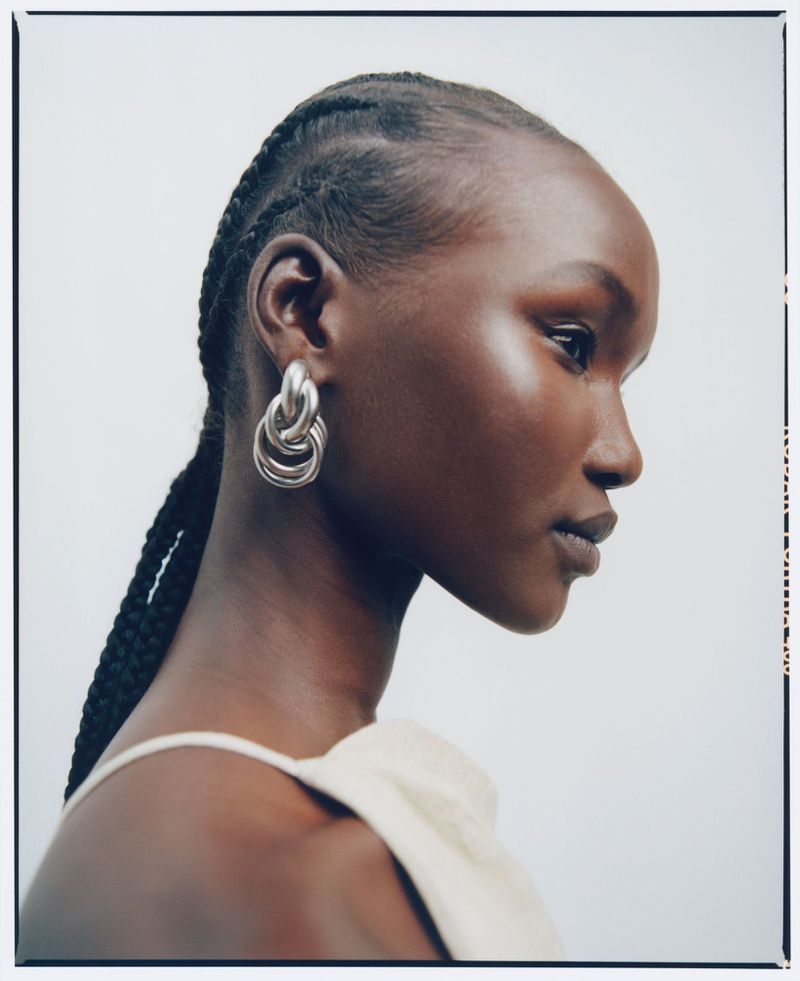 Close-up profile of an adult female with braided hair wearing large silver earrings against a light background in a studio setting.