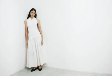 Model wearing a white halter top and long white skirt standing against a plain white studio corner.