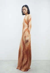 Model wearing a long-sleeved orange and brown patterned dress standing against a seamless white background.