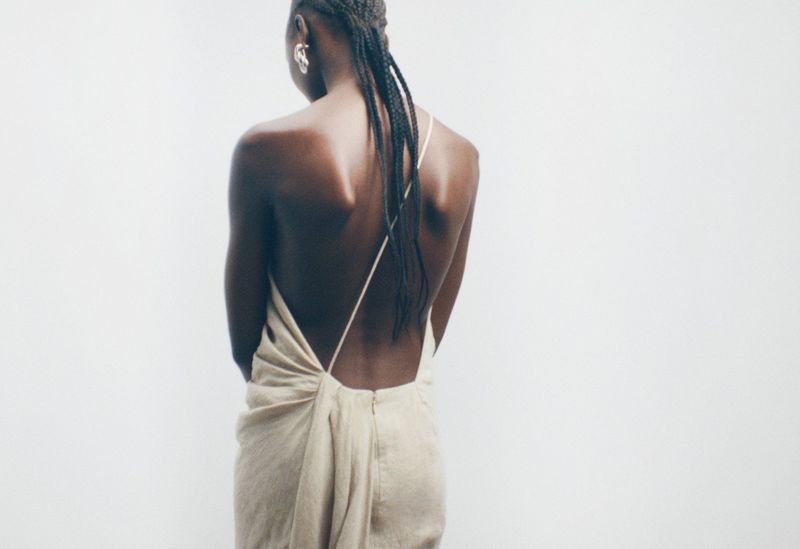 Model seen from behind wearing a cream backless dress against a plain white background, photographed by Maya Skelton for Tove.