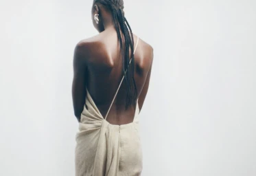 Model seen from behind wearing a cream backless dress against a plain white background, photographed by Maya Skelton for Tove.