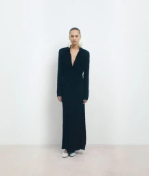 Model in a long black dress standing against a neutral white studio background for Tove Studio S/S 24.