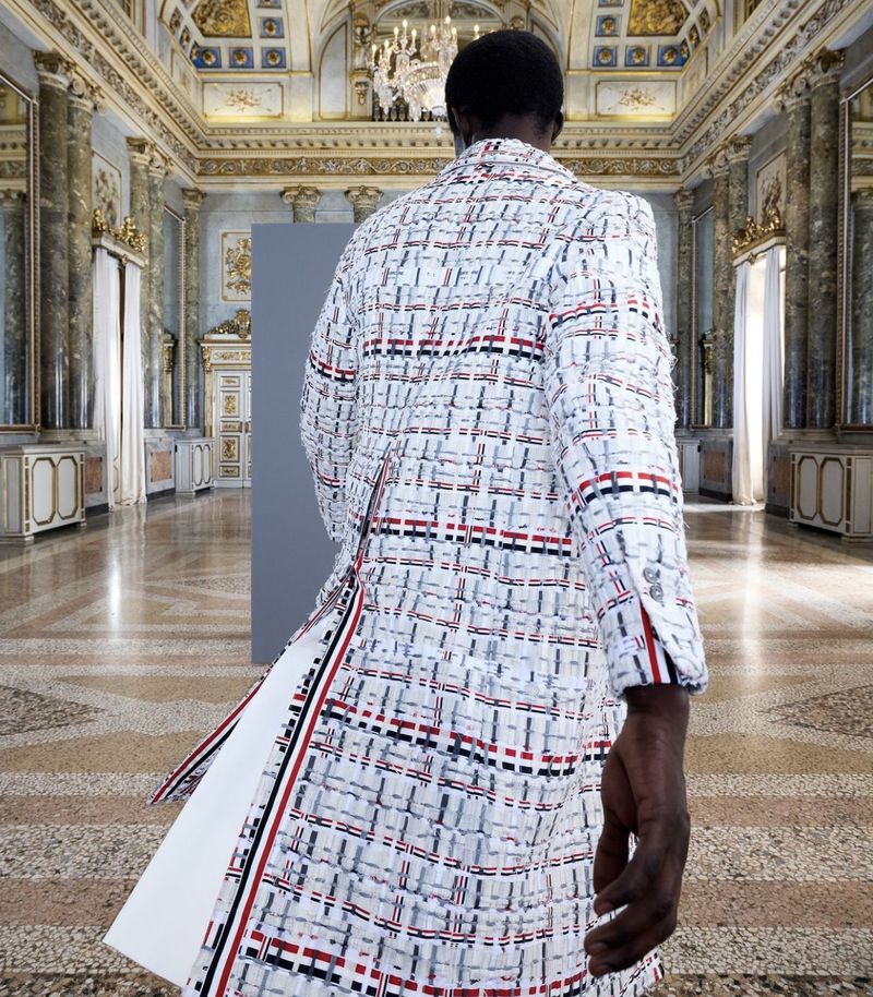 Back view of a Black male model in a tweed coat with red and blue stripes in an ornate interior with decorative walls and tiled floor.
