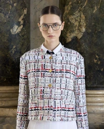 Model wearing a tweed jacket with red and blue stripes and round glasses against a marble column backdrop.