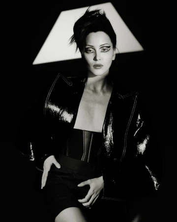 Monochrome portrait of an adult female model in a black patent leather jacket with dramatic eye makeup posing in a photo studio.