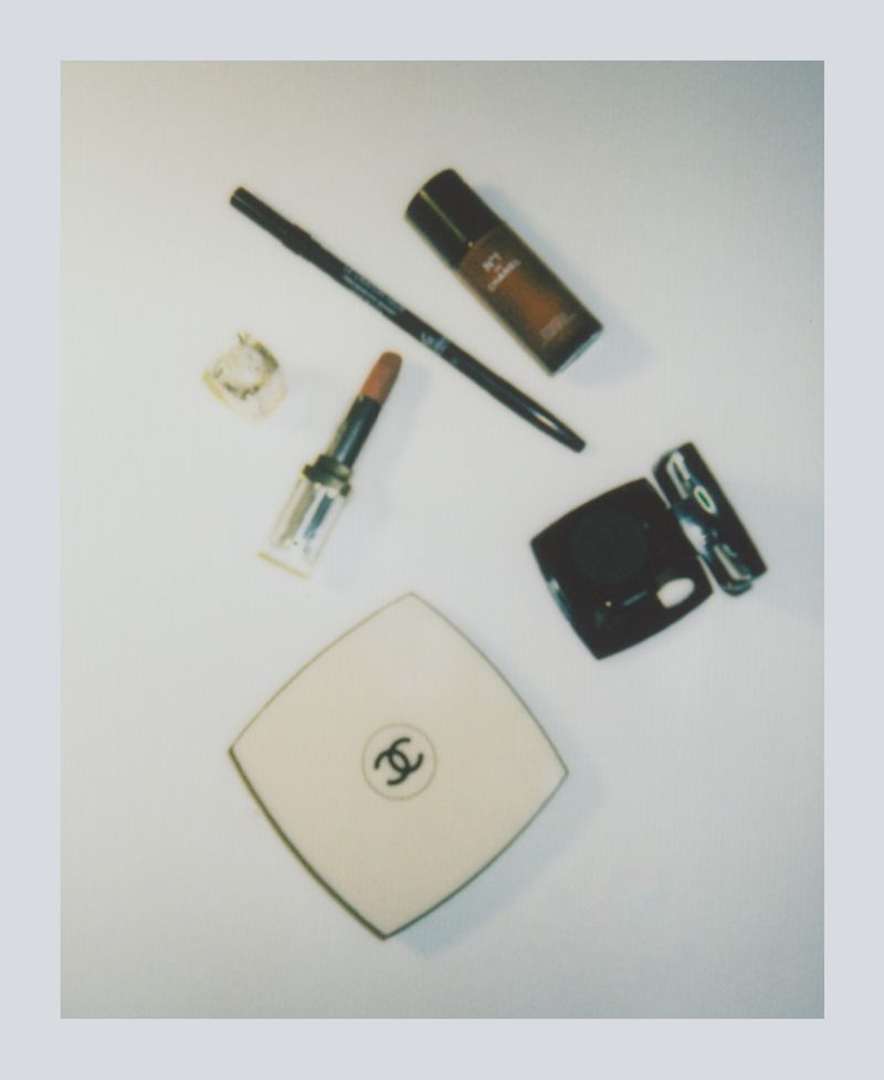 Still life shot of Chanel makeup products including lipstick, compact powder, foundation, and eyeliner on a white surface.