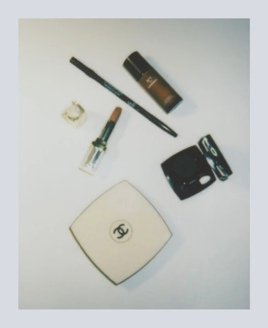 Still life shot of Chanel makeup products including lipstick, compact powder, foundation, and eyeliner on a white surface.