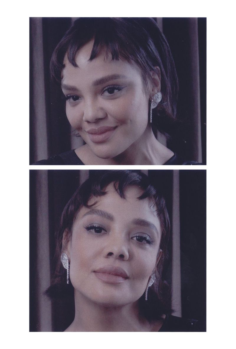 Close-up portrait of a woman with short dark hair and bangs, wearing sparkly earrings, against a dark striped background.
