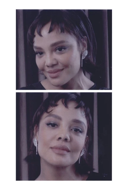 Close-up portrait of a woman with short dark hair and bangs, wearing sparkly earrings, against a dark striped background.