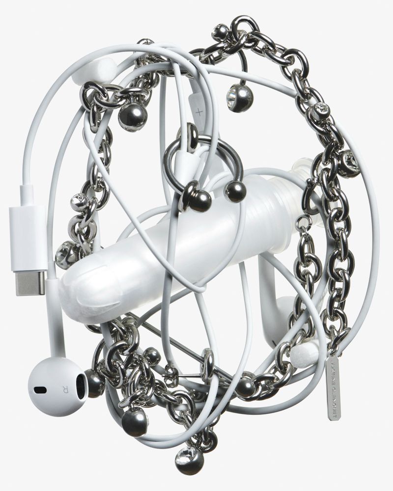 Close-up of white earphones and charger entangled with a silver metal chain, featuring hanging silver balls, against a plain white backdrop.