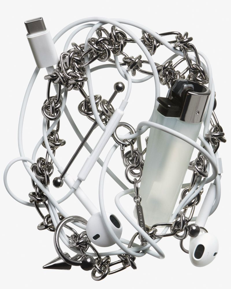 Still life of an assortment of everyday objects, including earbuds, a white USB-C cable, a lighter, and a silver metal chain.