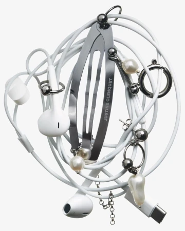 Still life of entangled white Apple earbuds and charging cable, with a metal hair clip and faux pearl jewelry on a white backdrop.