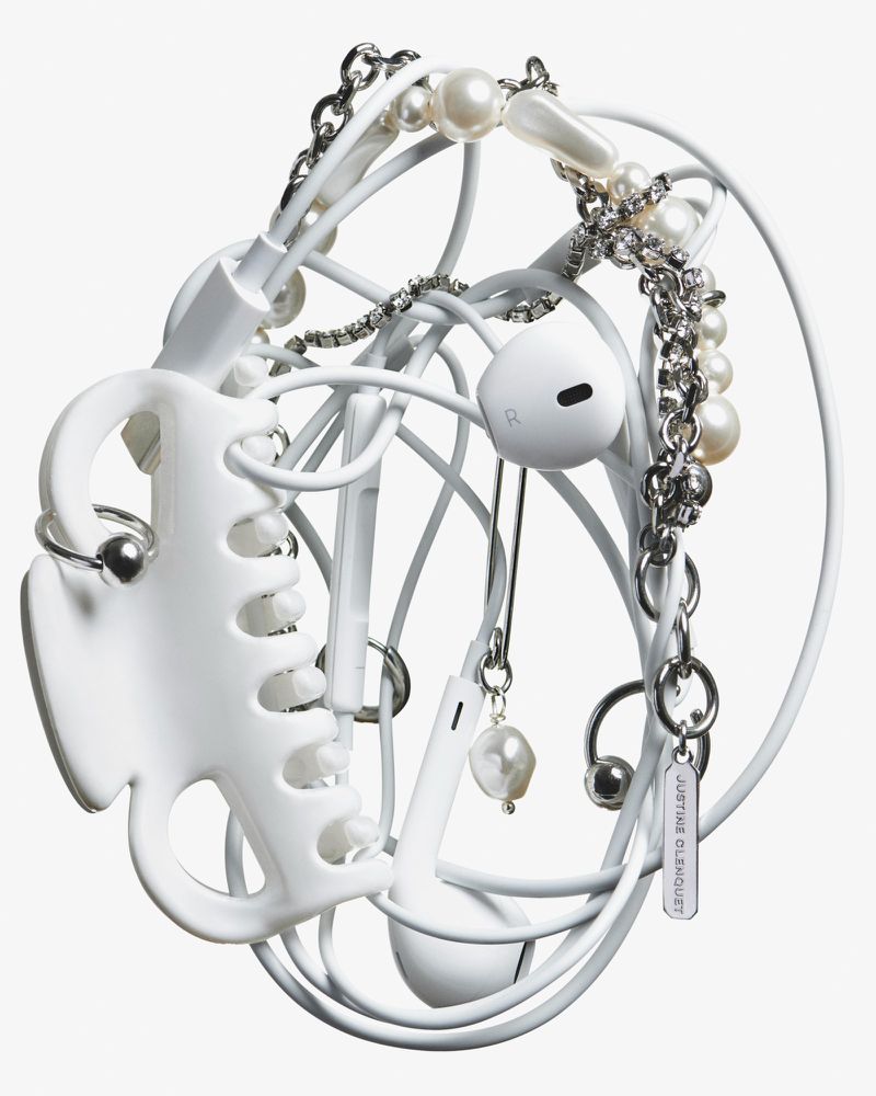 Still life of tangled white earphones with pearl and silver jewelry, and a white hair claw on a white background.