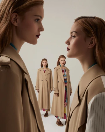 Fashion shot featuring two red-haired women in tan trench coats against a pale background, striking a pose that accentuates the clothing's style.