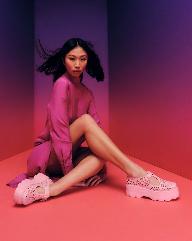 Fashion photo of an Asian female model with black hair posing in a studio wearing a pink dress and pink platform shoes.