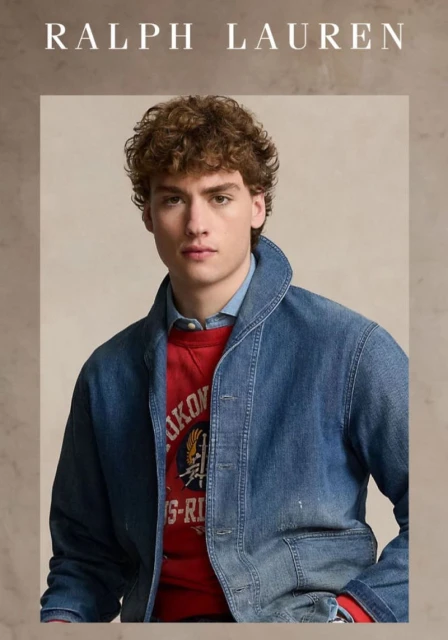 Portrait of a young male model with curly hair, wearing a red graphic sweatshirt and denim jacket, featured in a Ralph Lauren advertisement.