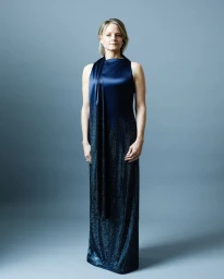 Jodie Foster wearing a dark blue shimmering gown standing against a grey studio seamless backdrop