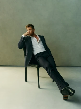 Adult man in suit poses on chair in studio. The subject is fair-skinned with short, light-brown hair and is dressed in business attire.
